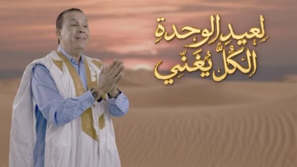 Abdelali El Ghaoui en daraâ sahraouie dans le désert, avec le titre « لعيد الوحدة الكل يغني » en calligraphie dorée